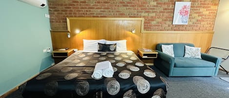 Una habitación de hotel con una cama grande, un cabecero de madera, un sillón verde y una pared de ladrillo.
