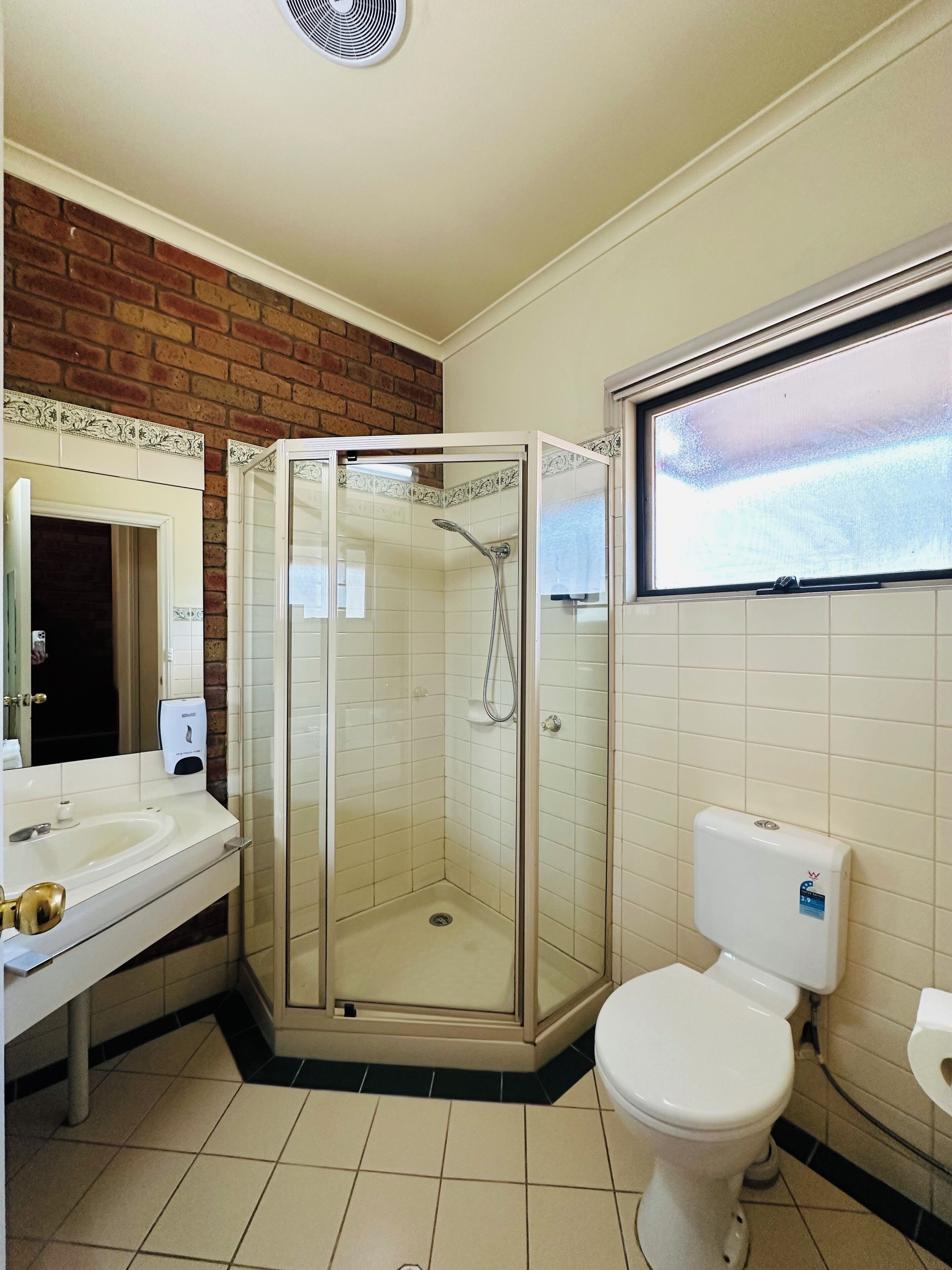 Un baño con ducha de vidrio, inodoro, lavamanos y ventana.