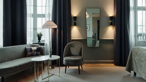 Una habitación de hotel moderna con sofá, sillón, mesa redonda y un espejo grande.
