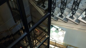 Un interior de varios niveles con barandillas de vidrio, suelo a cuadros y un arreglo floral en la planta baja.