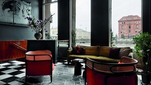 Un interior moderno con suelo a cuadros, un sofá, una silla roja y un ventanal con vistas a un edificio.