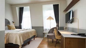 Una habitación de hotel con cama, escritorio, silla, lámpara y televisión.