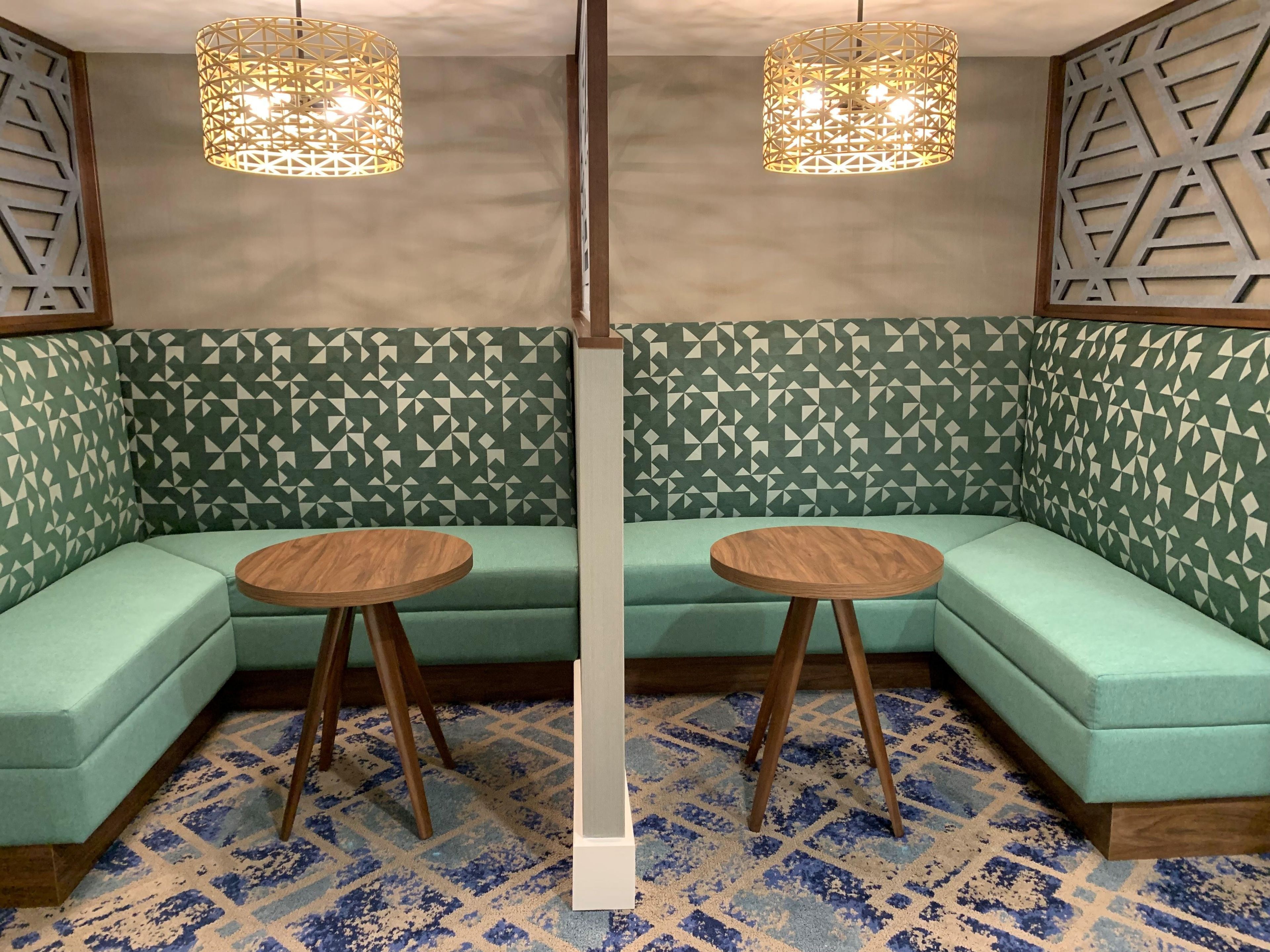 A room with a green patterned sofa, two wooden tables, and geometric wall decor.