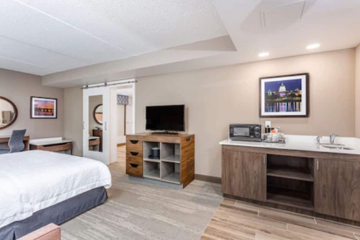A hotel room with a bed, a TV, a wooden cabinet, and a kitchenette.