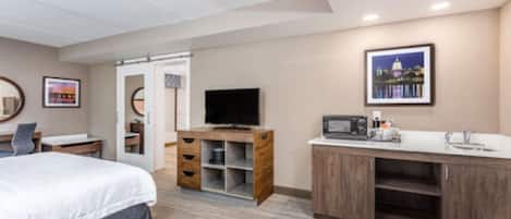 A hotel room with a bed, a TV, a wooden cabinet, and a kitchenette.