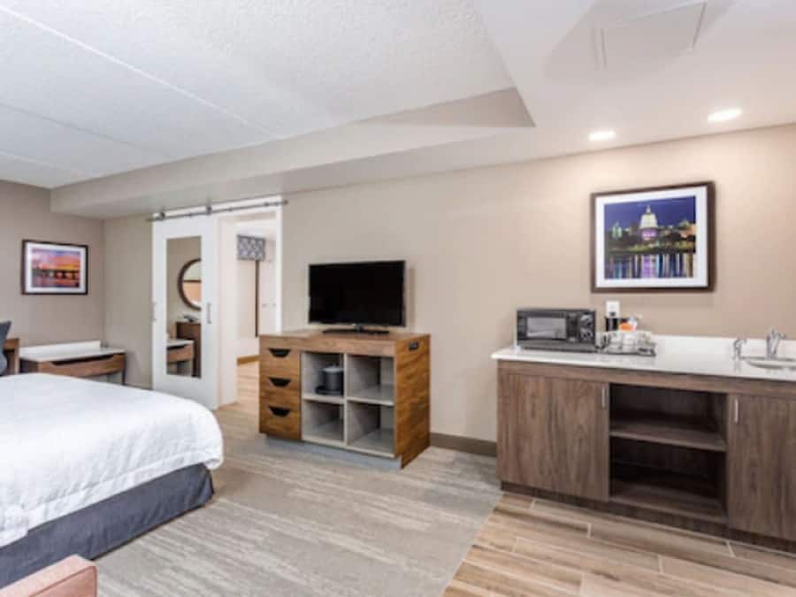A hotel room with a bed, a TV, a wooden cabinet, and a kitchenette.