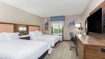 A hotel room with two beds, a desk, a chair, a television, and artwork on the walls.