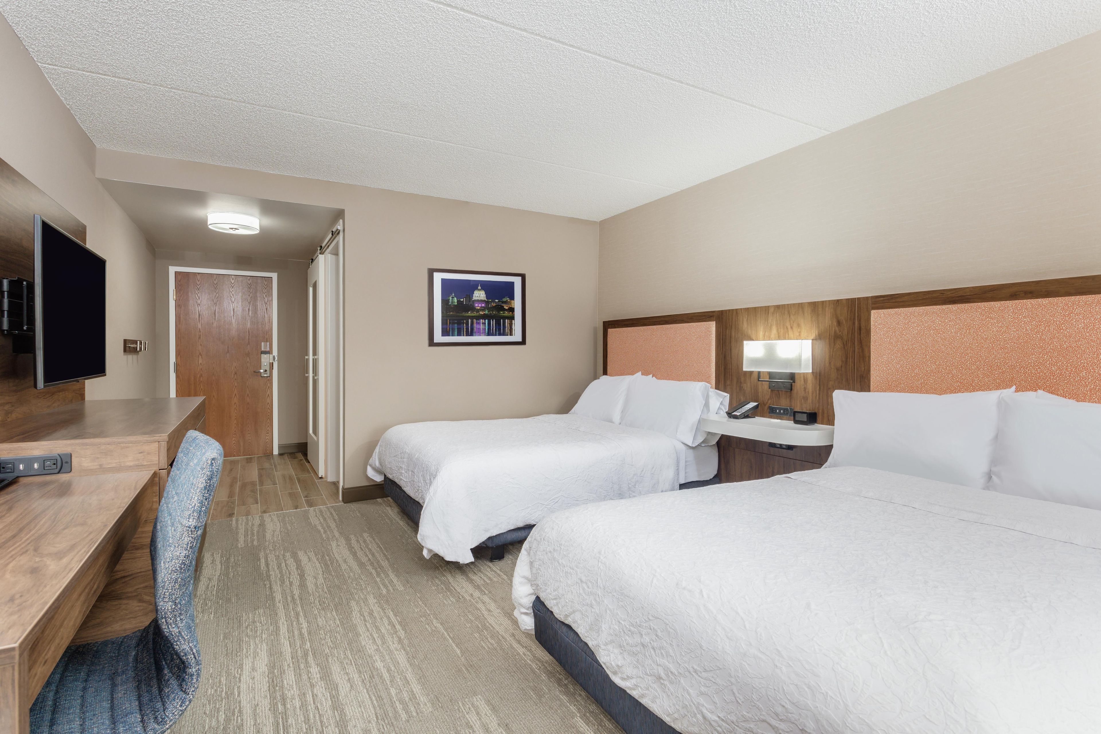 A hotel room with two beds, a desk, a chair, a television, and a framed picture on the wall.