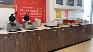 Uma bancada de cozinha com máquinas de waffle, pratos de waffle e acompanhamentos.