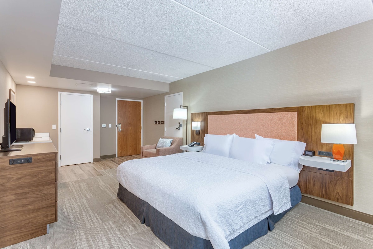 A hotel room with a large bed, a desk with a computer, a TV, and a bathroom with a shower and toilet.