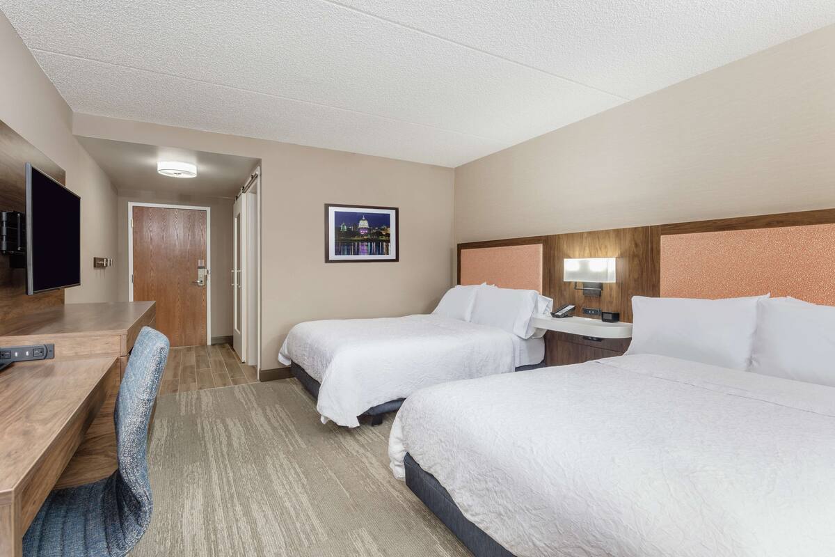 A hotel room with two beds, a desk with a chair, a television, and a framed picture on the wall.