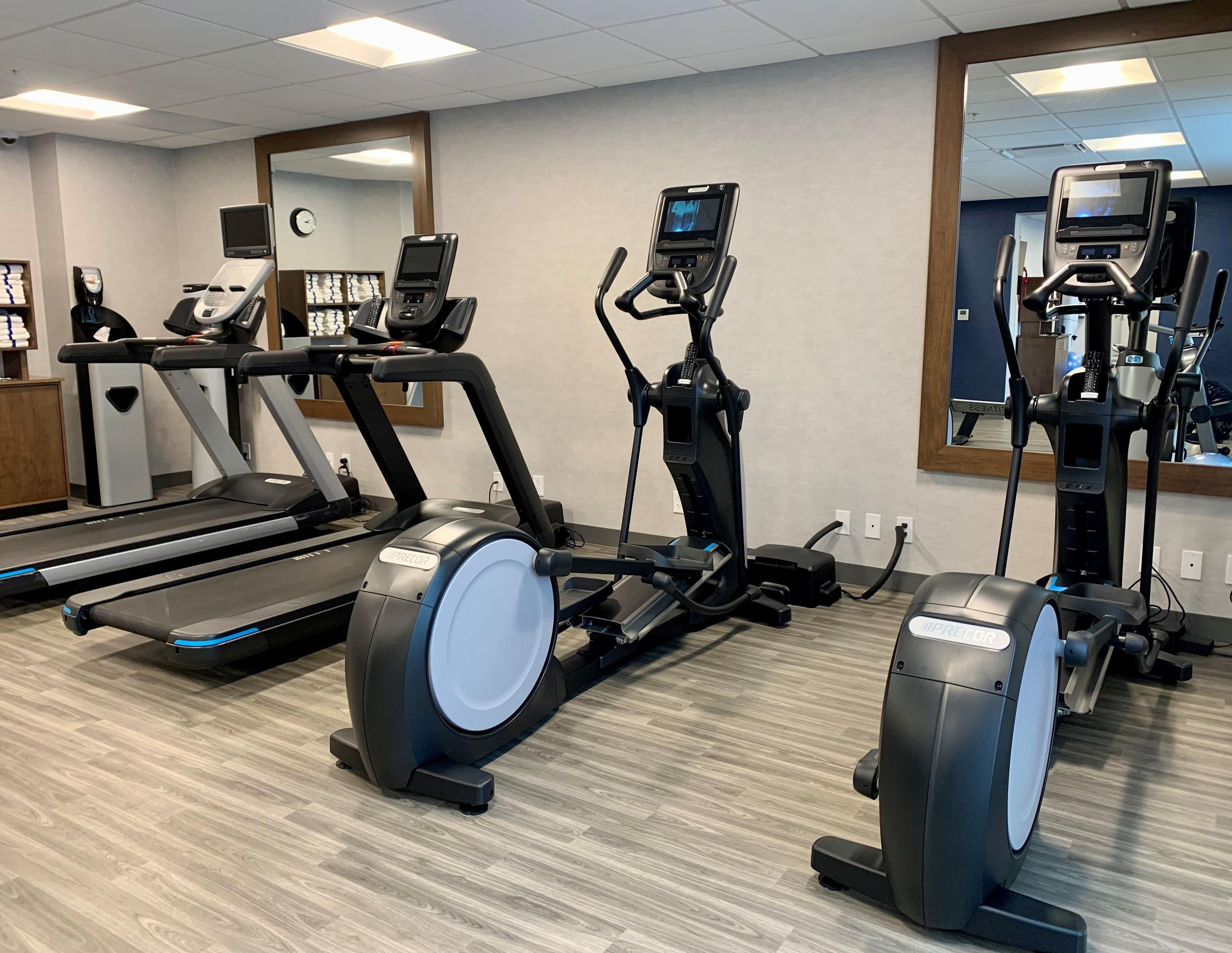 Et fitnessrum med løbebånd, crosstrainere og et spejl.