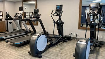 Et fitnessrum med løbebånd, crosstrainere og et spejl.