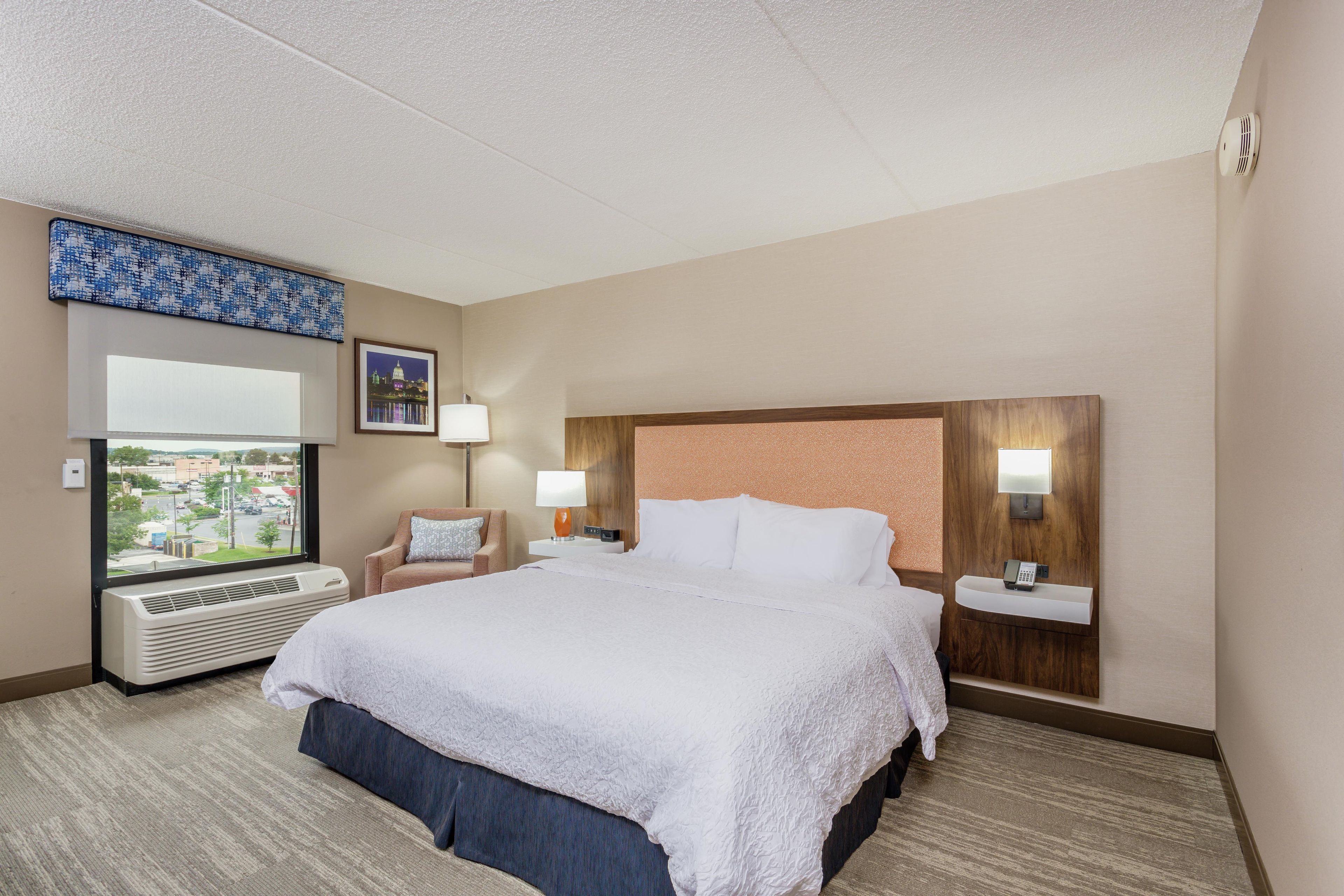 Une chambre d’hôtel avec un grand lit, une fenêtre donnant sur un beau paysage, un bureau avec un téléphone et un radiateur fixé au mur.