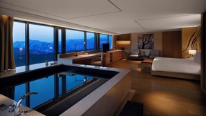 A modern hotel room with a large window, a bathtub, a sofa, and a desk with a television. - BanyanTree Club & Spa Seoul (Seoul)