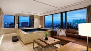 A modern hotel room with a large bathtub, a sofa, a coffee table, and a view of the cityscape. - BanyanTree Club & Spa Seoul (Seoul)