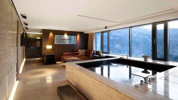 A modern spa room with a large hot tub, a sofa, and a painting on the wall.