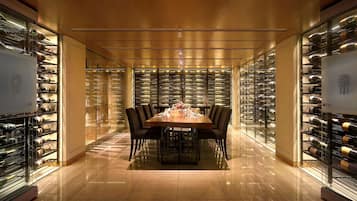 A wine cellar with a polished floor, a dining table with chairs, and glass-fronted wine racks on either side.