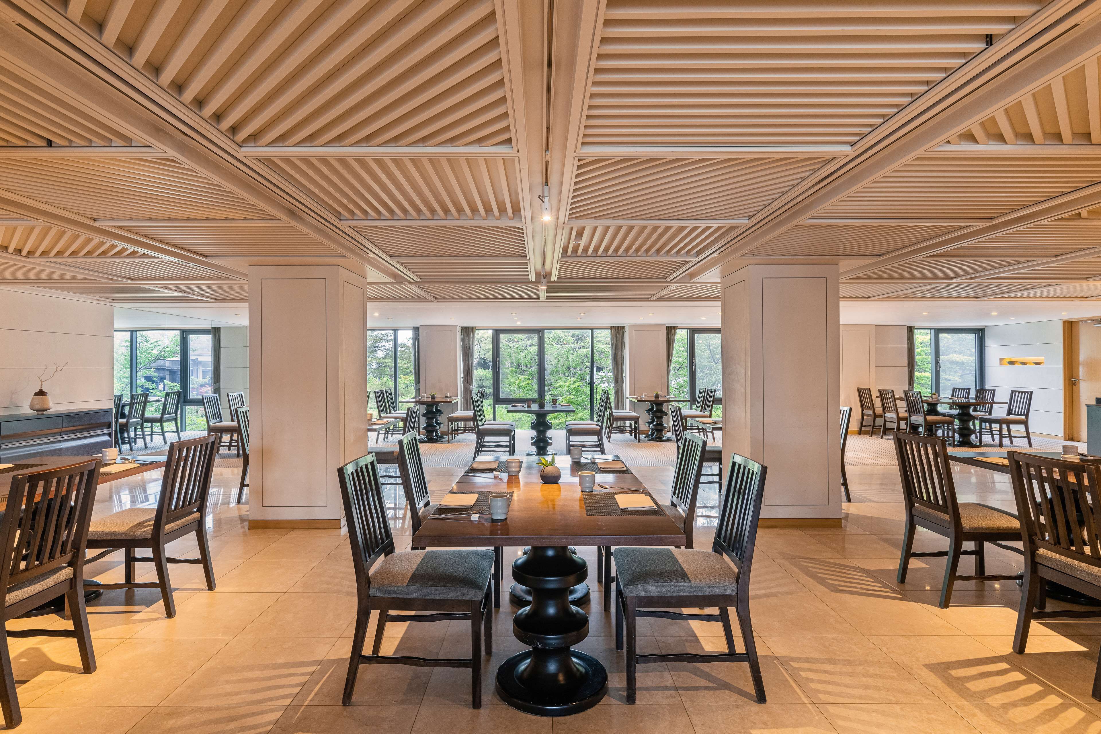 A spacious dining area with multiple tables and chairs, large windows, and a modern ceiling design.