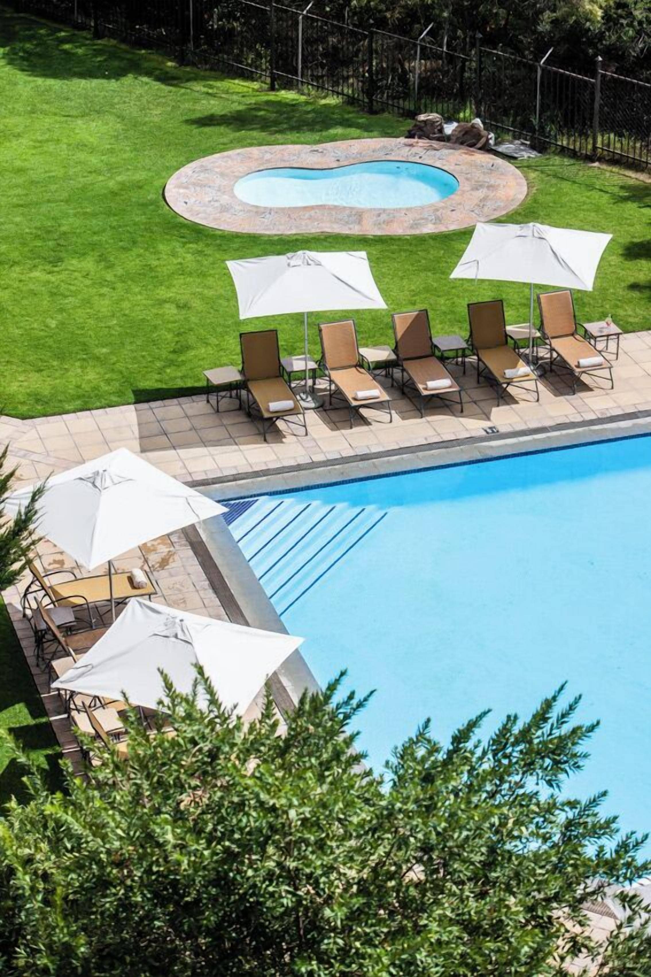 A swimming pool with lounge chairs and umbrellas, surrounded by a well-maintained lawn and a stone hot tub.