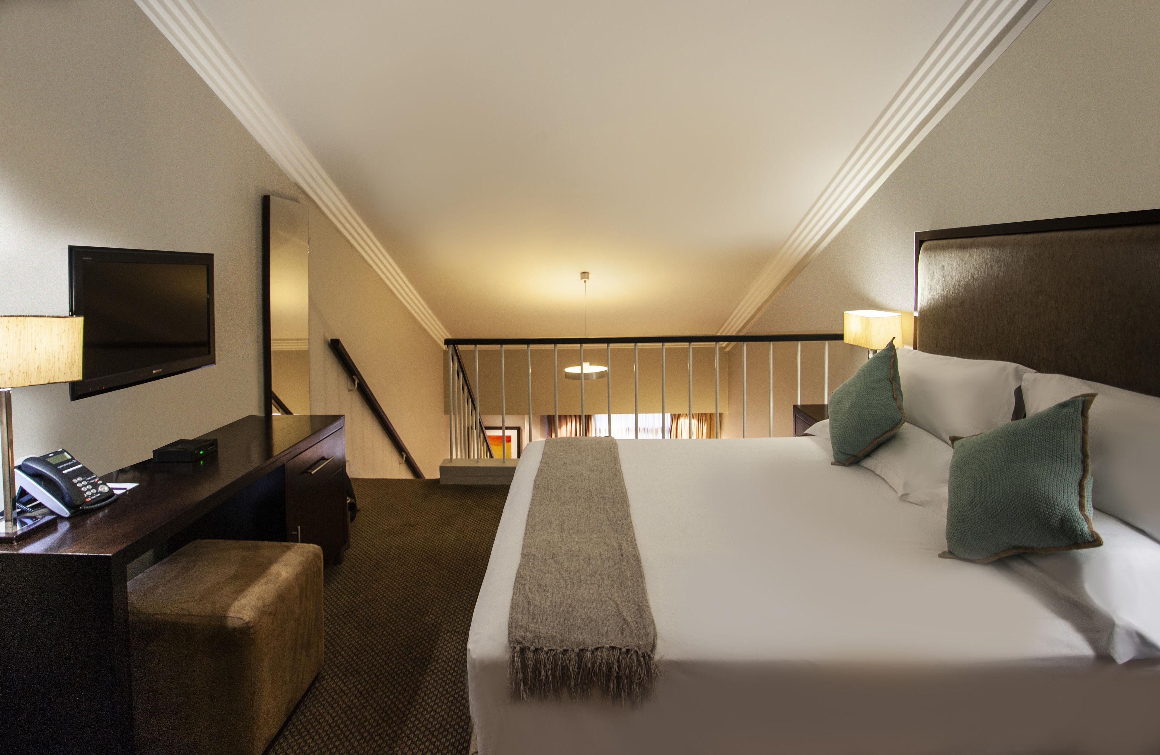 A hotel room with a bed, bedside lamps, a desk with a telephone, and a television.