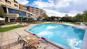 A swimming pool with lounge chairs and umbrellas, surrounded by a landscaped garden and a building with multiple balconies. - Avani Lesotho Hotel & Casino (Maseru)