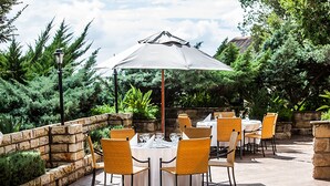 Eine Terrasse im Freien mit Steinmauern, Korbstühlen und runden Tischen, die zum Essen bereitstehen.