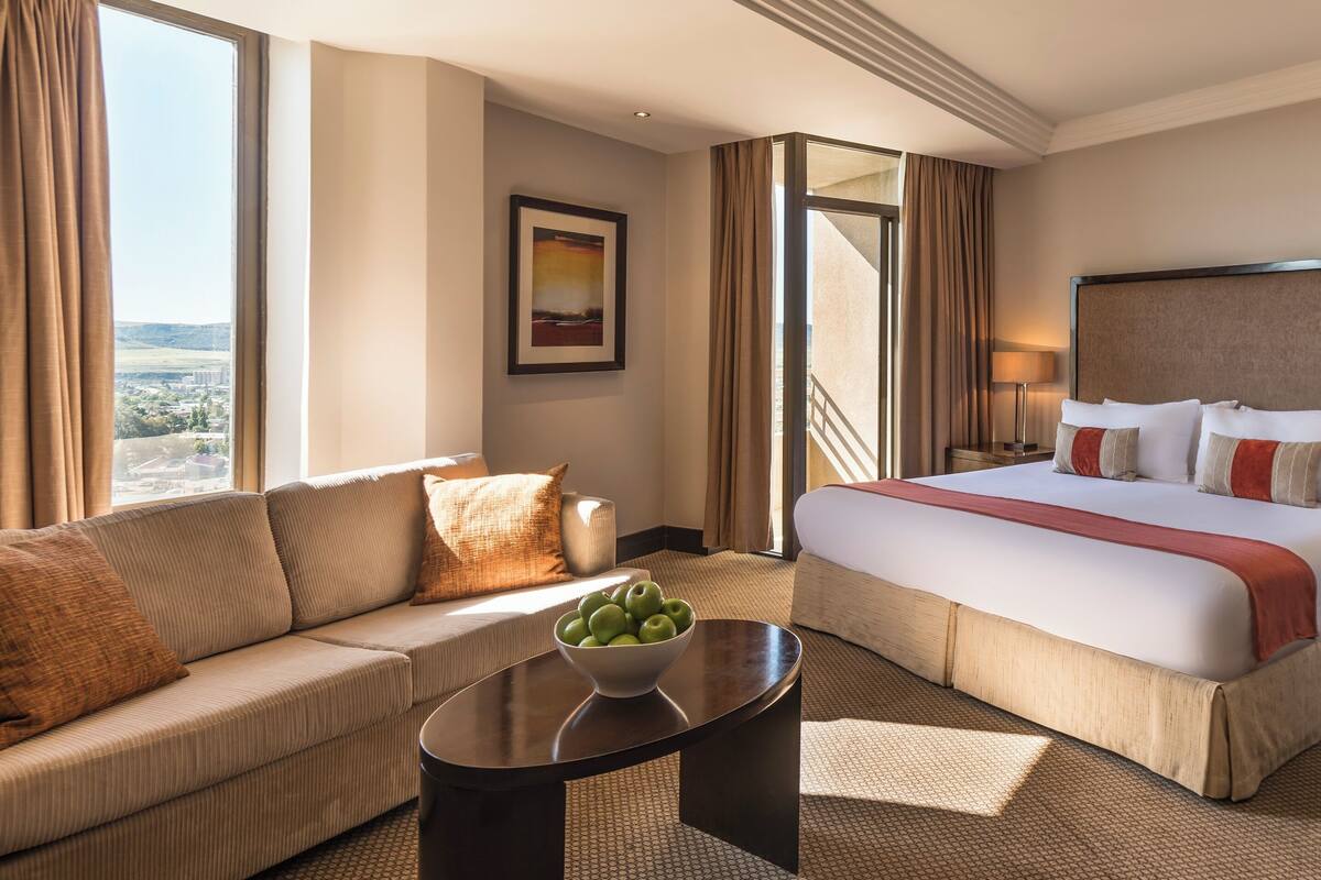 Una habitación de hotel con una cama grande, un sofá, una mesa de centro con manzanas y un cuadro en la pared.