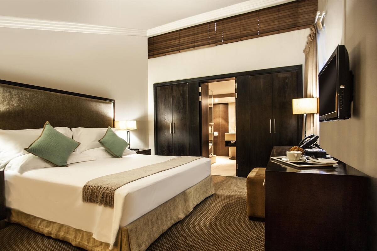 Habitación de hotel con una cama grande, un escritorio con lámpara, un televisor y un armario.