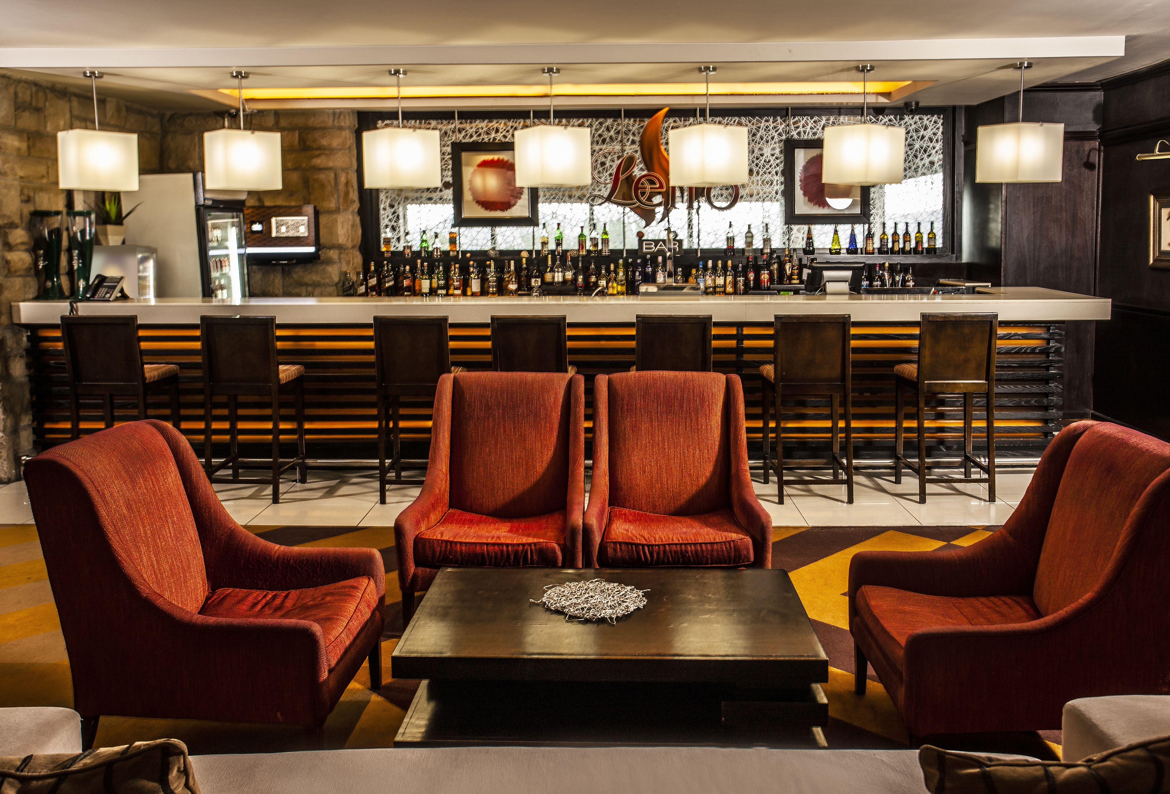 A bar area with a long counter, multiple bar stools, and a seating area with two red upholstered chairs and a table.