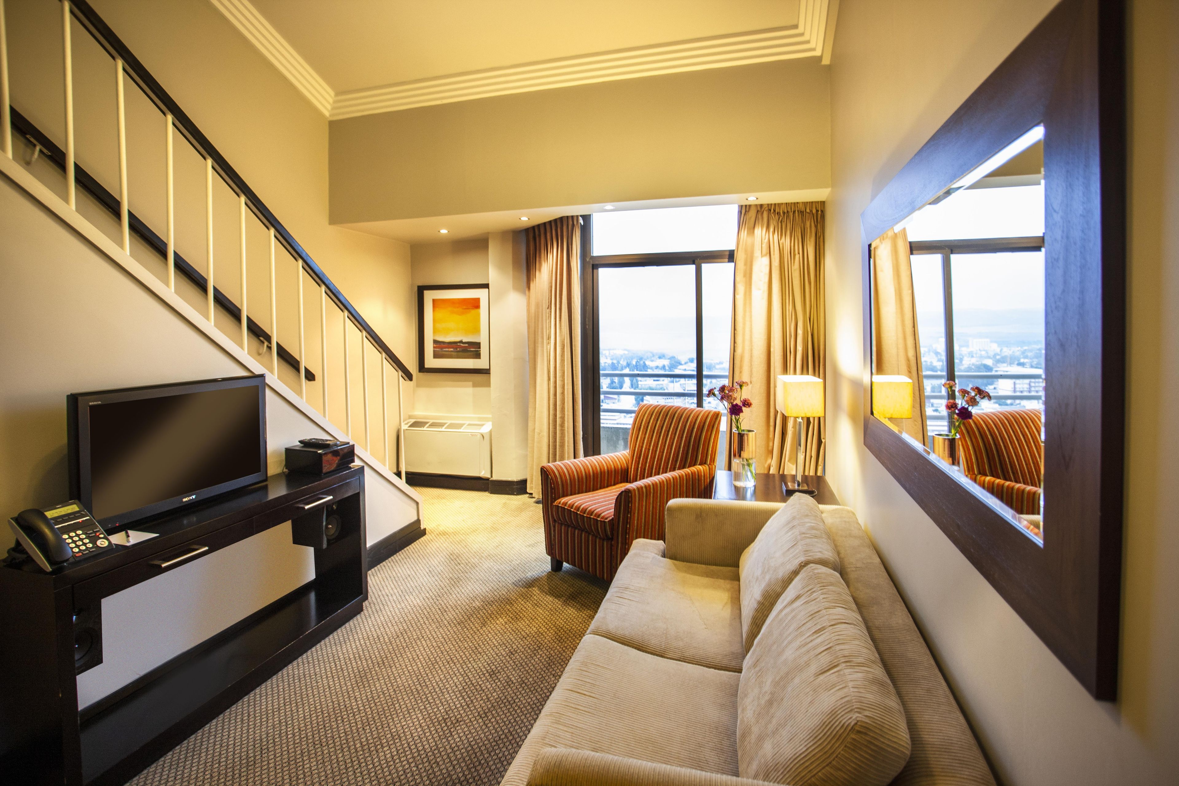 Habitación de hotel con sofá, sillones, televisor, escritorio y escalera.