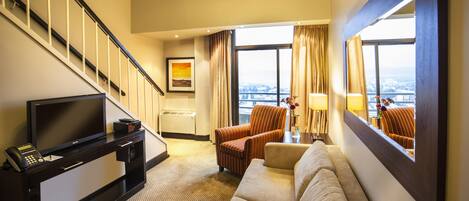 Habitación de hotel con sofá, sillones, televisor, escritorio y escalera.