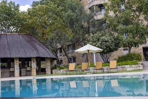 Una piscina con sillones de playa y sombrillas, rodeada de edificios de piedra y árboles.