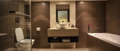 Un baño moderno con cabina de ducha de vidrio, inodoro blanco, tocador con espejo y bañera.