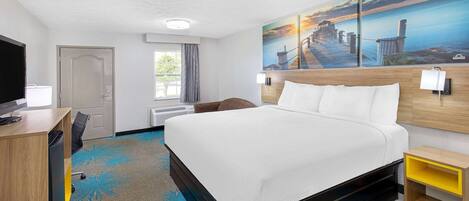 A hotel room with a large bed, a desk with a chair, a TV, a painting on the wall, and a window with curtains.