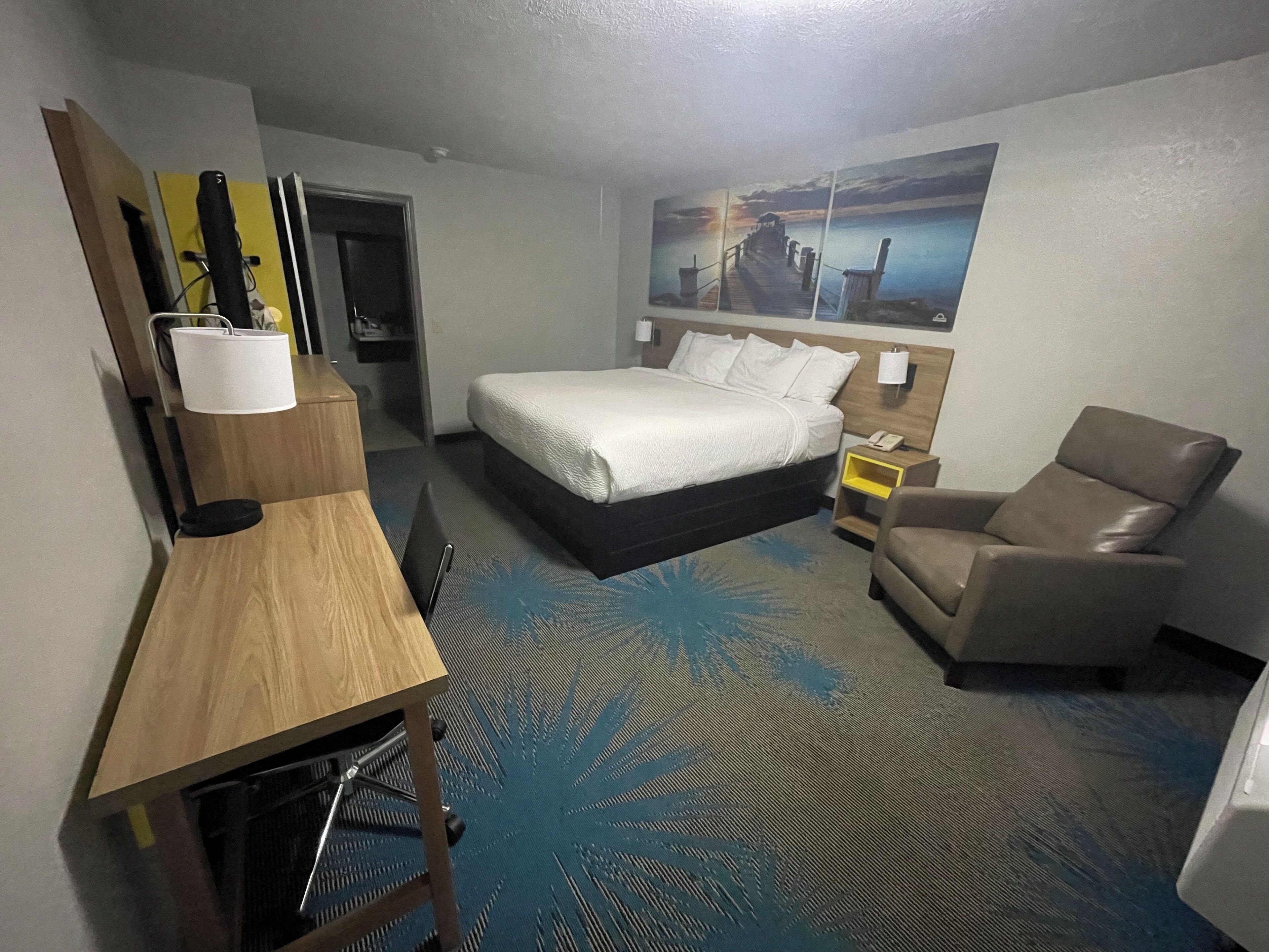 A hotel room with a bed, a desk, a chair, and a painting on the wall.