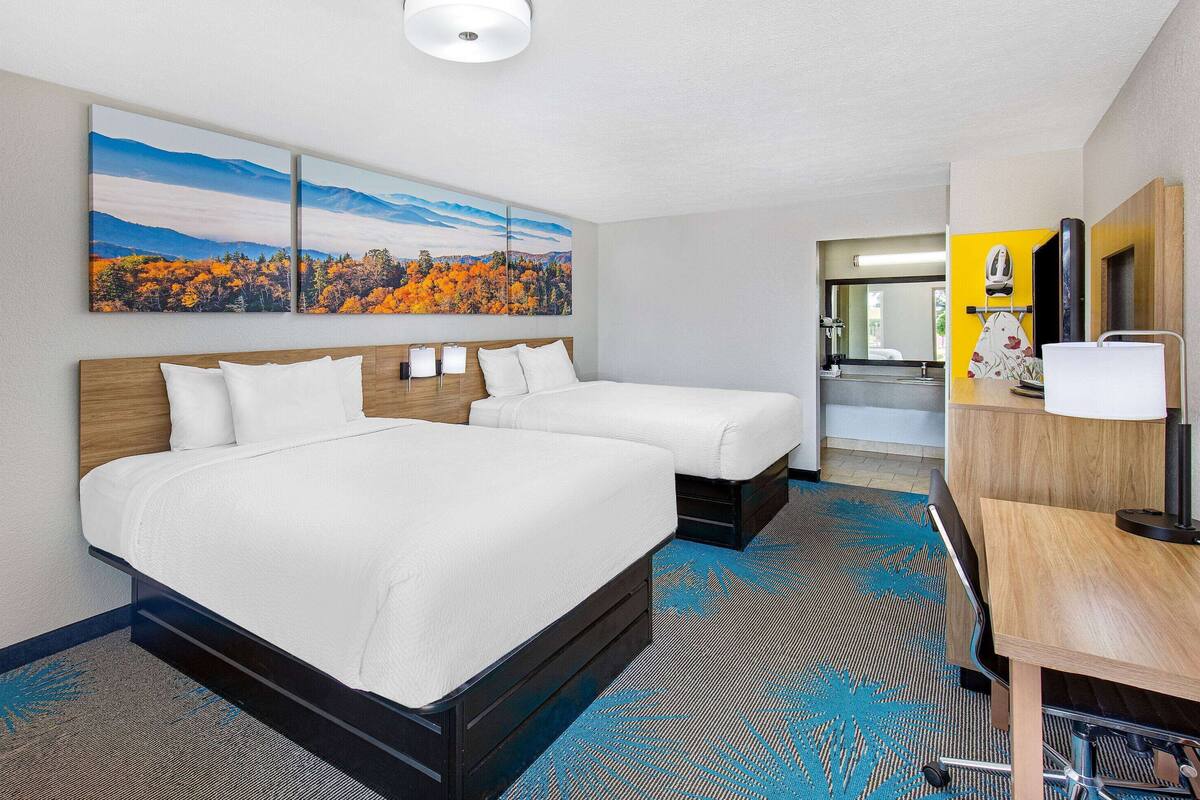 A hotel room with two beds, a desk, and a bathroom visible through an open door.
