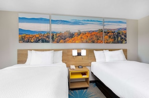 Une chambre d’hôtel avec deux lits, une tête de lit en bois, une table de chevet avec un téléphone et un livre, et un grand tableau représentant un paysage au-dessus des lits.