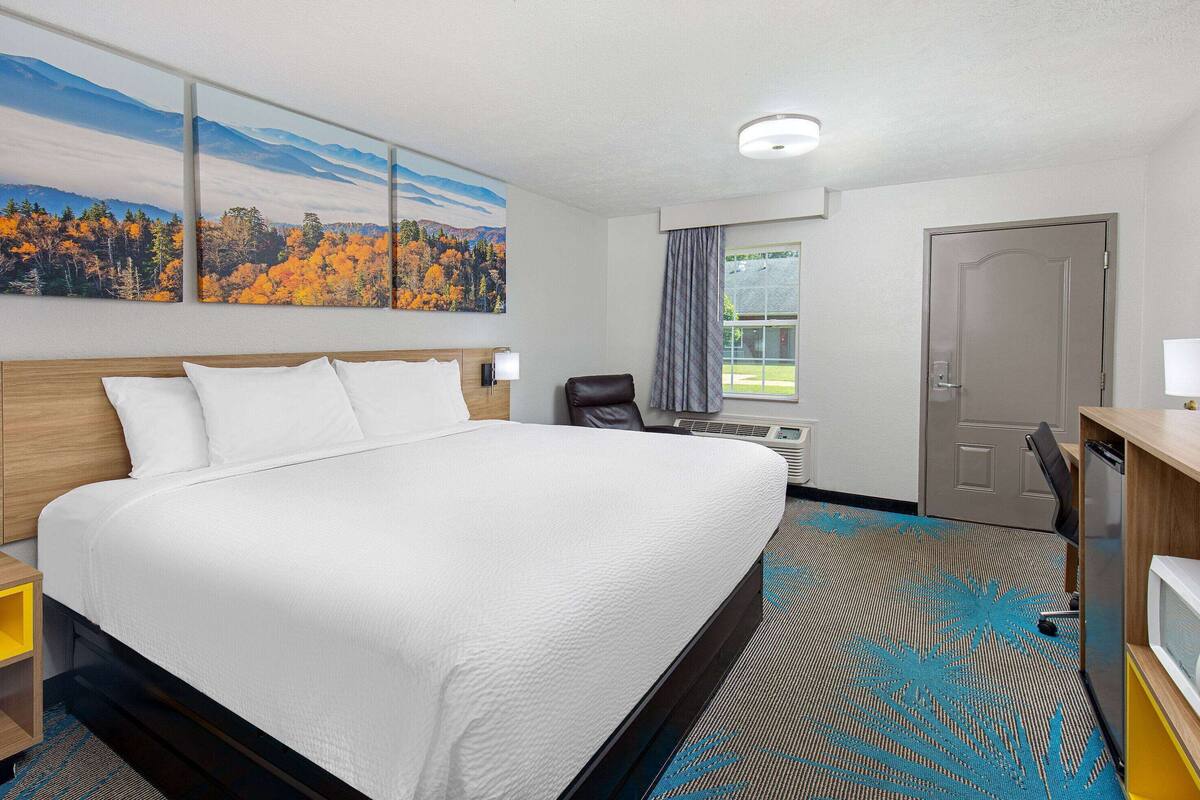 A hotel room with a large bed, a desk with a computer, a chair, and a window with curtains.
