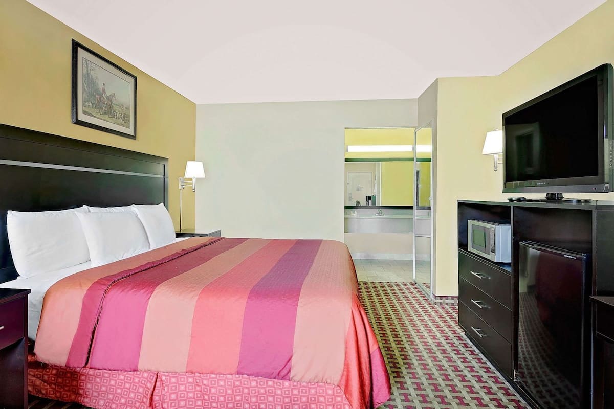 A hotel room with a bed, a television, a desk, and a bathroom visible through an open door.