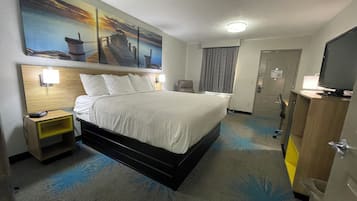 A hotel room with a bed, a nightstand, a desk, a television, and a painting on the wall.