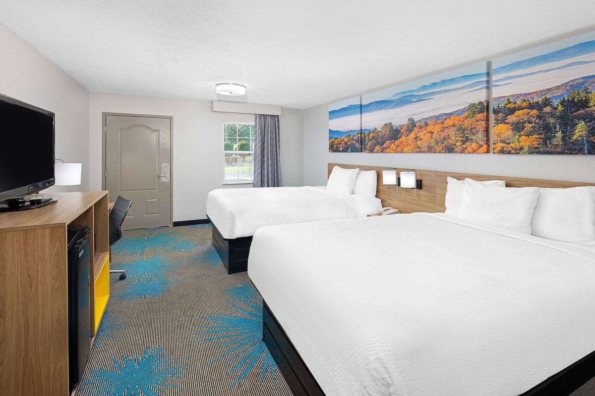 A hotel room with two beds, a TV, and a painting of a forest.