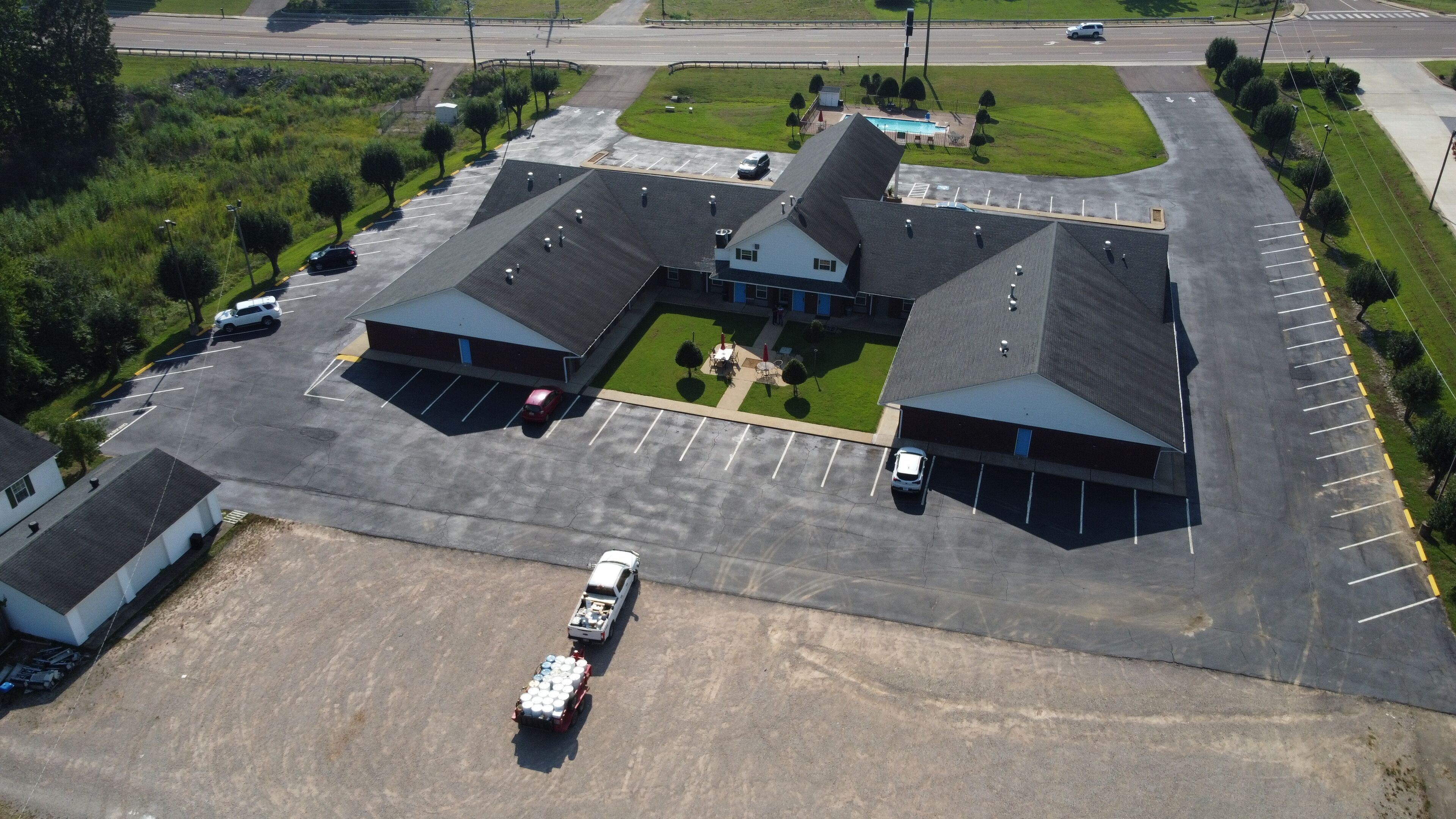 An aerial view of a parking lot with multiple buildings, including a large building with a sloped roof and a smaller adjacent structure.