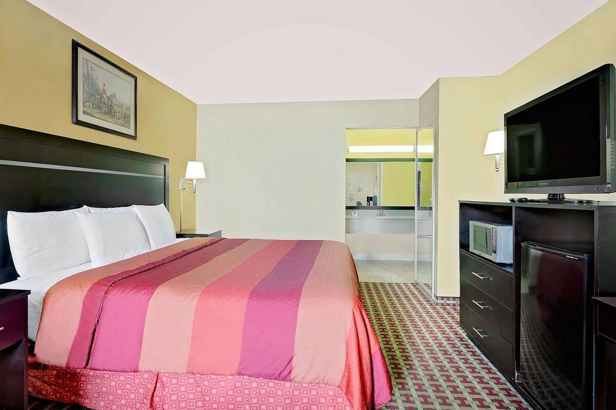 A hotel room with a bed, a television, a desk, and a bathroom visible through an open door.