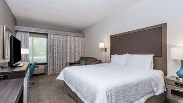 Quarto de hotel com uma cama grande, uma escrivaninha com computador, uma cadeira e uma televisão.
