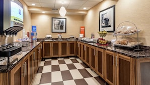 A hotel kitchen with a checkered floor, wooden cabinets, a coffee machine, and a food display.