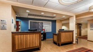 A hotel reception area with wooden reception desks, a blue wall with an 'explore' poster, and a sign indicating pet policy.