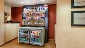A hotel breakfast area with a refrigerated display case and a wall-mounted shelf with snacks.