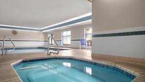 An indoor swimming pool with a tiled edge, a metal ladder, and a chair near the window. - Days Inn & Suites by Wyndham Airport Albuquerque (Albuquerque)