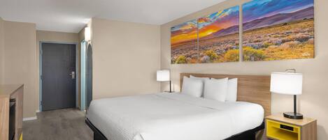 Una habitación de hotel con una cama, mesitas de noche, un escritorio, una silla y un cuadro grande de un paisaje en la pared.